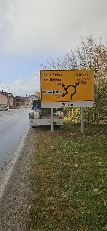 Žuti putokazni prometni znak uz cestu s oznakom kružnog toka